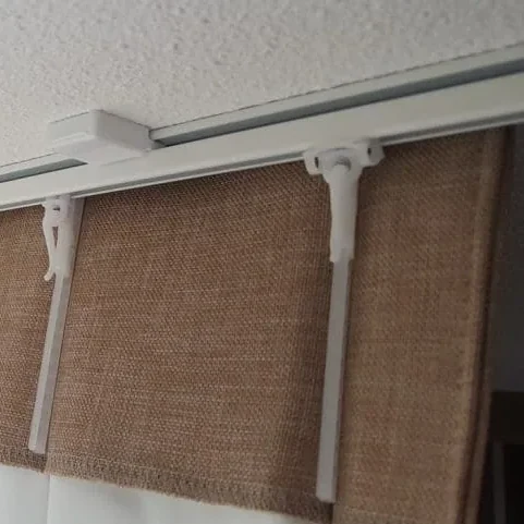 Vierkante detailfoto van een witte gordijnrail aan het plafond met gordijnhaken