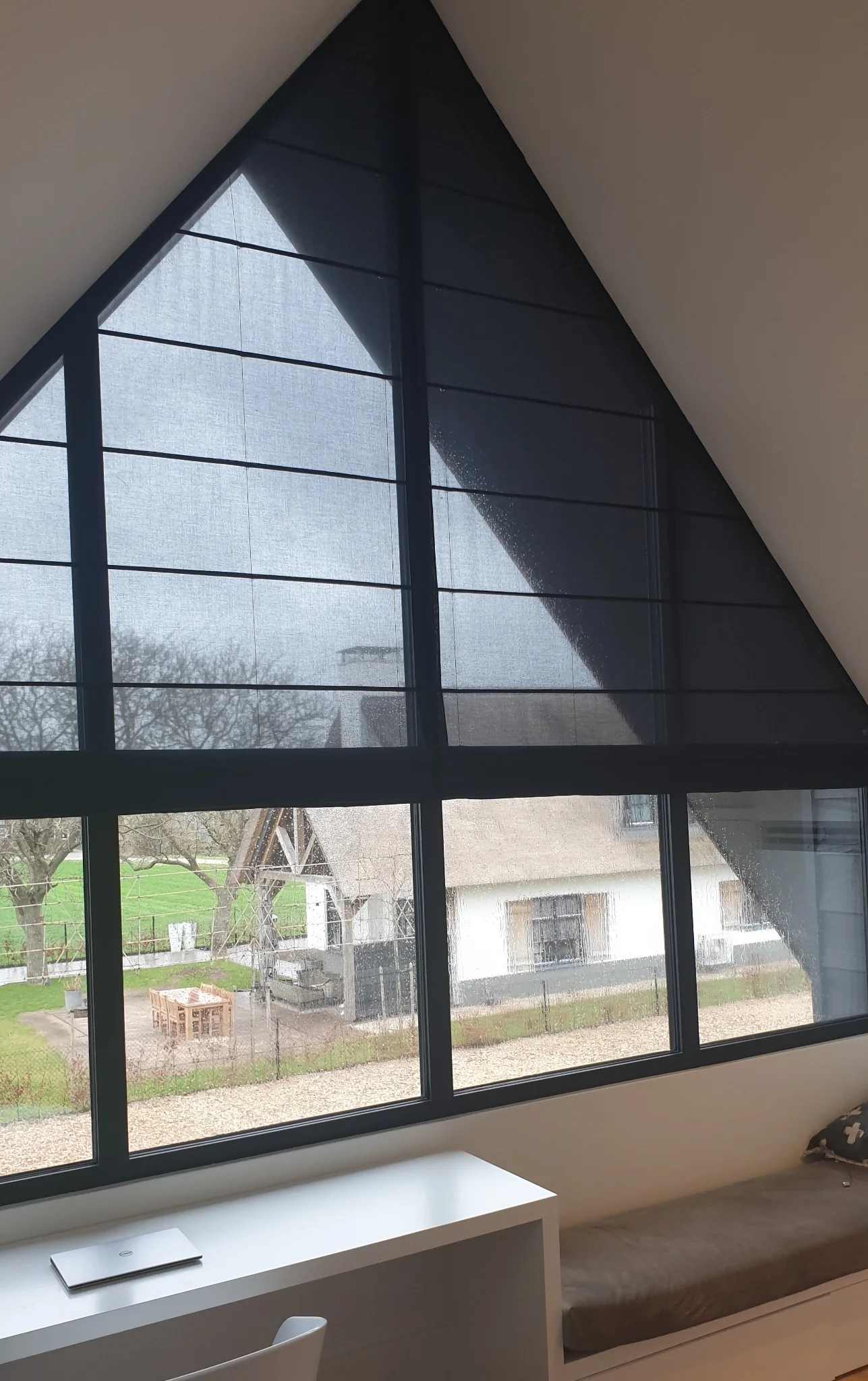 Schuine vouwgordijnen op maat langs een zwarte puntvormige raamconstructie