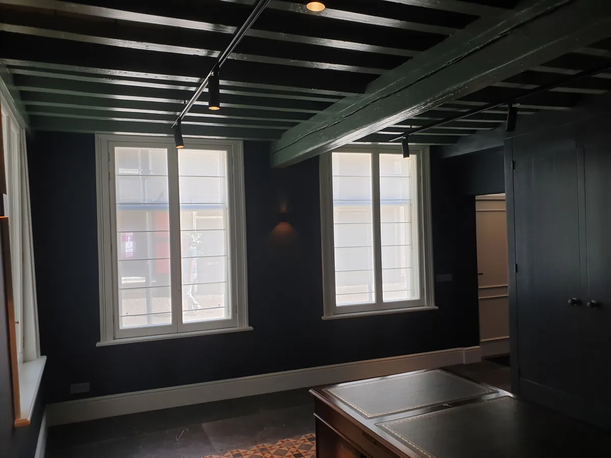 Roomwitte transparante vouwgordijnen achter voorzetramen in een donkere klassieke kamer